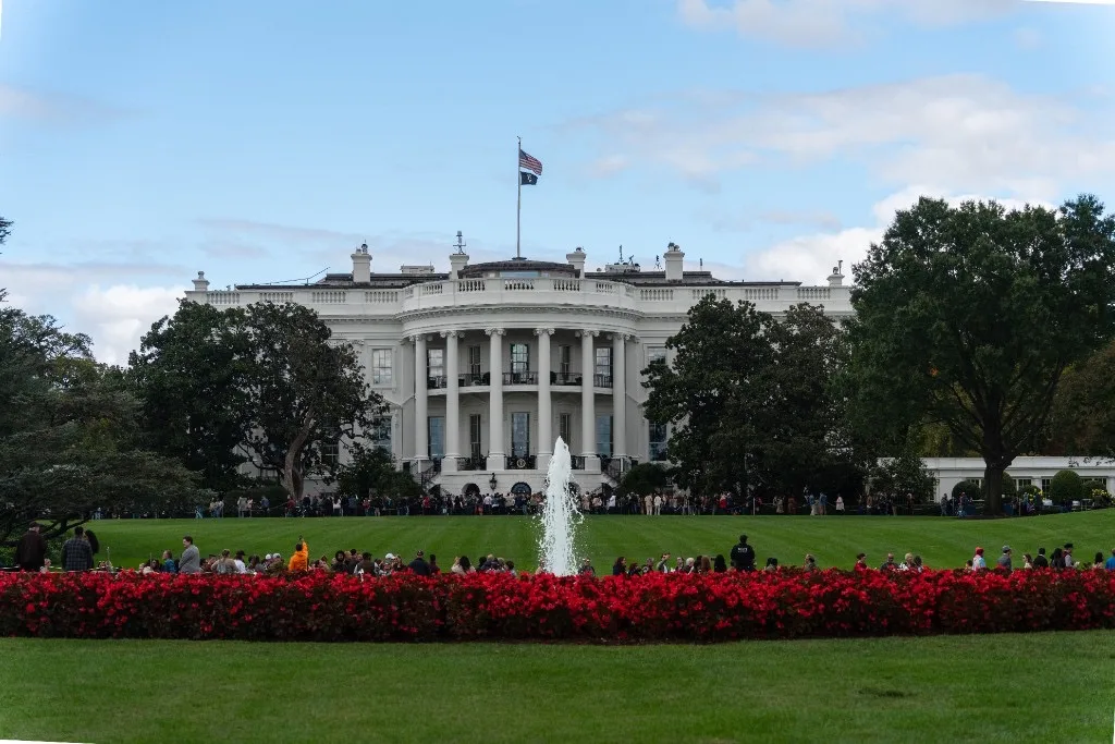 South Portico of the White House with red flower beds, fountain and visitors on the South Lawn under a partly cloudy sky